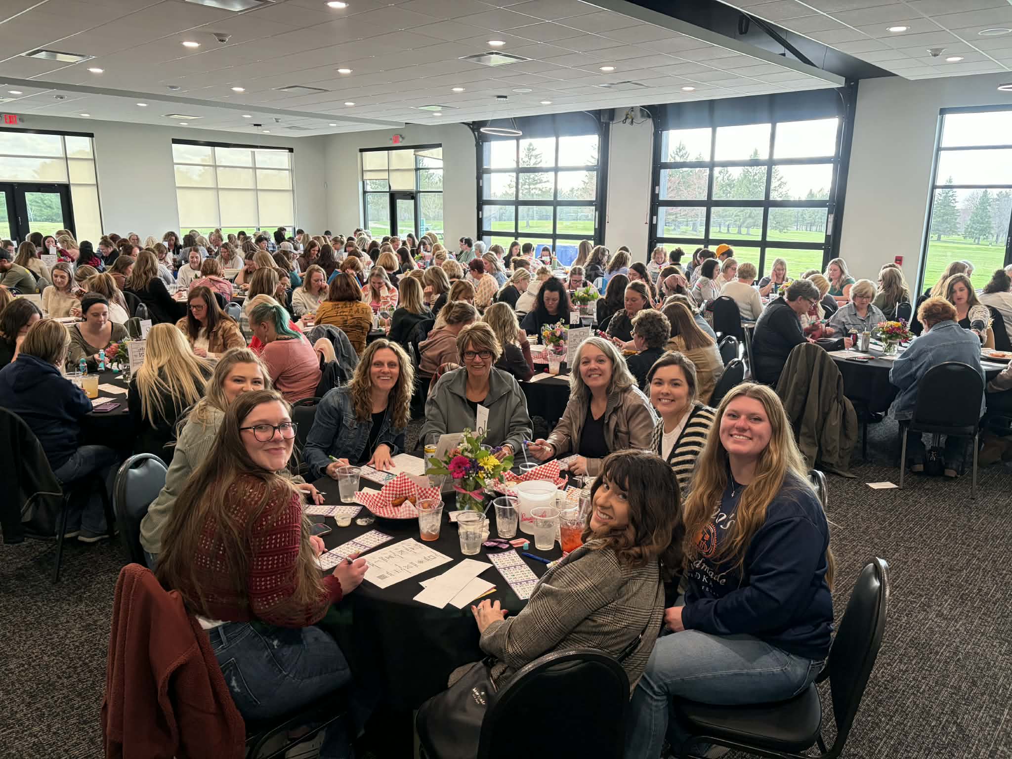Packed banquet hall of attendees at a Cadott Purse Bingo night, with a group of friends smiling in the foreground