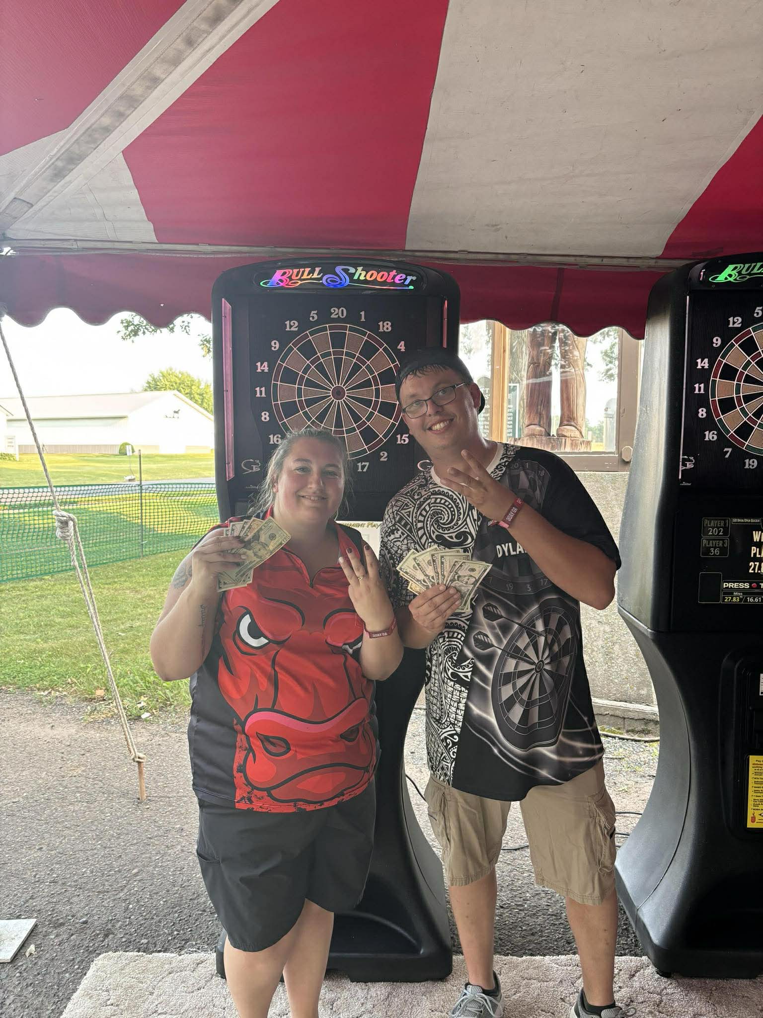 Dart tournament winners holding cash prizes at the Bull Shooter boards