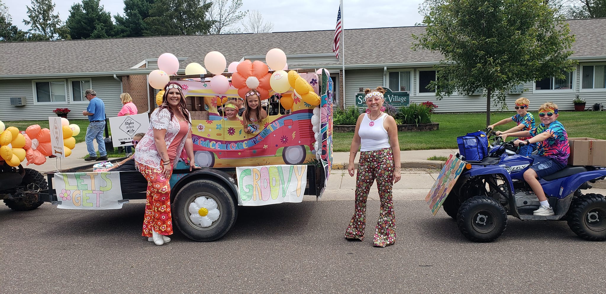 Styles on Main 1970s-themed parade float with women in vibrant outfits, balloons, and bright colors